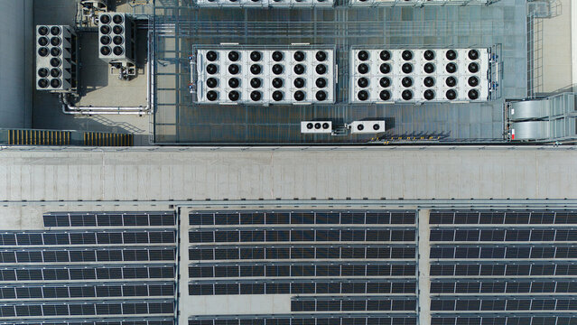 Aerial view of industrial rooftop featuring multiple ventilation cooling units, heat exchangers, HVAC fans, and rows of solar panels in Luton, England, United Kingdom.