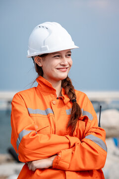 Female Refinery Engineer Smiling with Arms Crossed in Orange Protective Coveralls and a White Hard Hat during Work at an Outdoor Petrochemical Industrial Facility Worksite