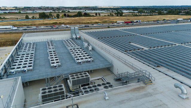 Aerial view of ventilation cooling units, heat exchangers and HVAC fans installed on a large industrial rooftop with a highway in the background in Luton, England, United Kingdom.