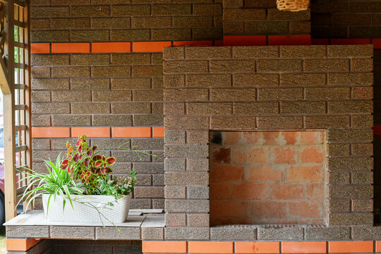 Rustic outdoor brick fireplace with textured brown masonry, orange brick accents, and decorative potted plants on a covered patio