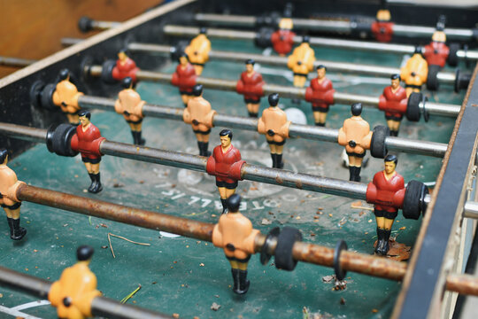 Close-up of an old, weathered foosball table with red and yellow player figurines outdoors. Selective focus. 