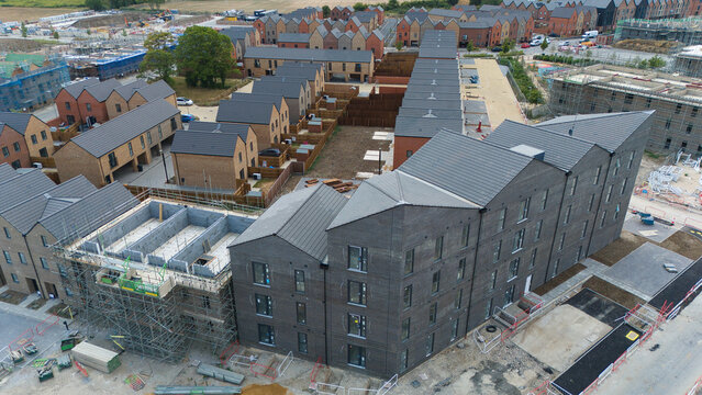 Aerial view of new residential housing construction featuring modern brick buildings with dark tiled roofs and ongoing development work in a suburban area in Luton, England, United Kingdom.