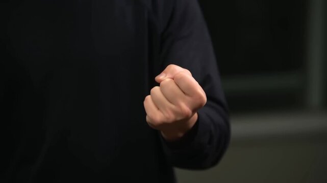 Clenched human fist held forward in dark indoor setting with black sleeve