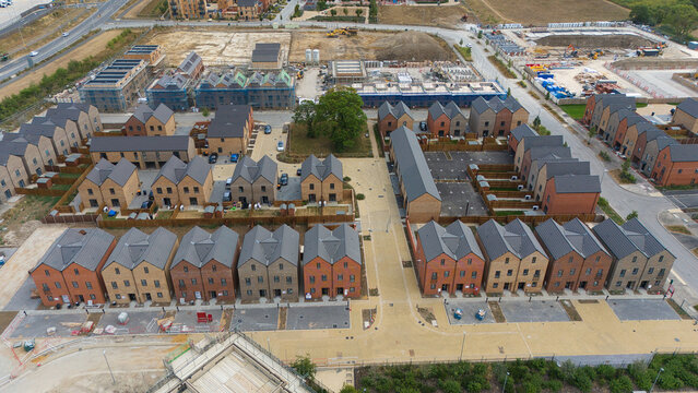 Aerial view of new residential housing construction featuring rows of modern brick houses with dark roofs, paved walkways, and surrounding development areas in Luton, England, United Kingdom.