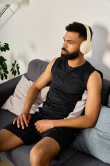 Fototapeta premium A stylish young african american man enjoys music at home, sitting on a comfortable couch.