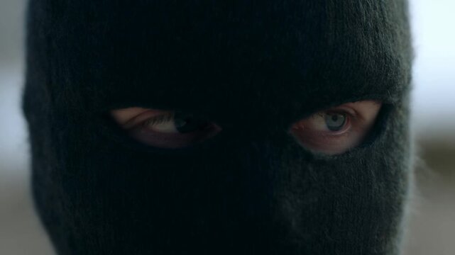 Masked person staring sideways in closeup against softly blurred indoor background