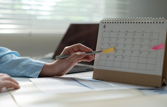 Business professional marking a desk calendar while reviewing reports, representing schedule planning, deadline management, appointment organization, productivity, project timing and office workflow.