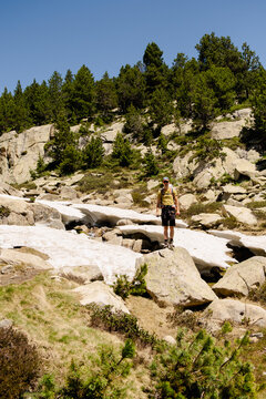 UGC Solo trekker standing on rocks beside lingering snow in Pyrenees