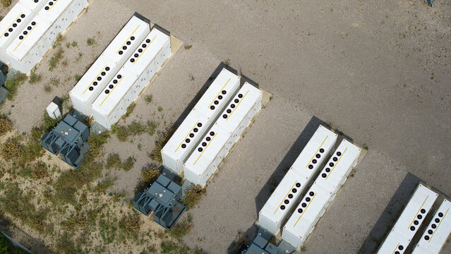 Aerial view of the BESS Battery energy park near the M1, featuring rows of white energy storage containers with cooling fans on gravel ground in Sundon, England, United Kingdom.