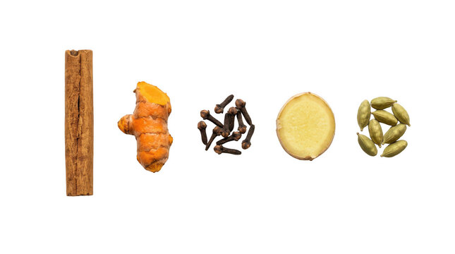 Cinnamon stick turmeric root cloves ginger slice and green cardamom pods arranged in a row