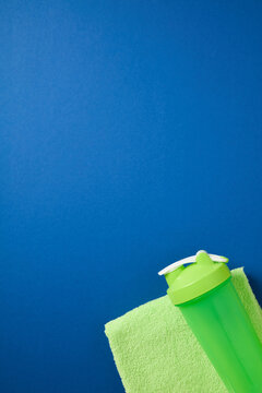 Green shaker bottle and towel on blue background with space.