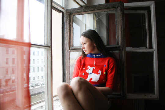A girl sitting near the window and looking outside