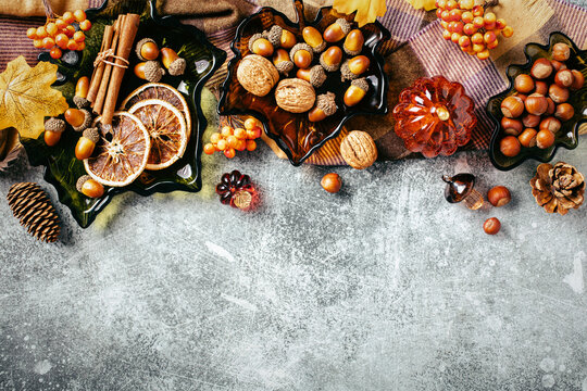 Autumn top border flat lay with glass plates, acorns, nuts and spices on stone table.