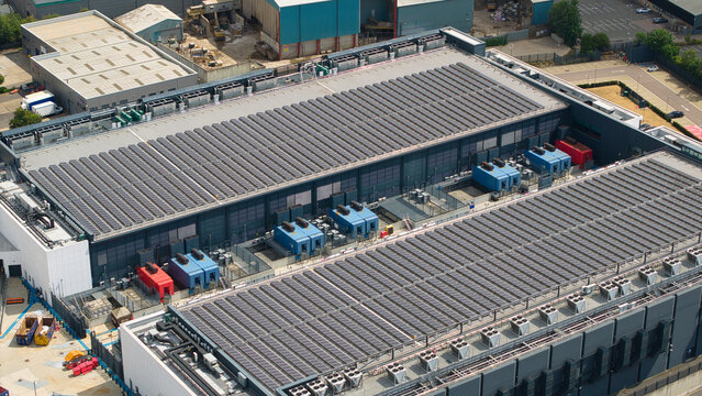 Aerial view of a large data center facility featuring extensive rooftop solar panel arrays and industrial HVAC server cooling units in Hemel Hempstead, England, United Kingdom.