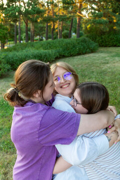 Three young women hugging in park at sunset