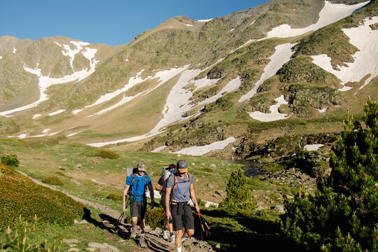 UGC Men hiking past alpine lake and snowy slopes in Pyrenees