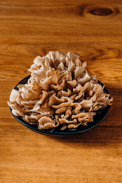 Fresh maitake mushrooms in a dark bowl on a wooden table