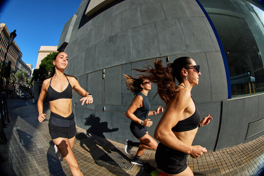 Women run on city street near modern building during sunny morni