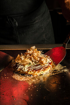 Cooking okonomiyaki on a teppan grill with metal spatulas