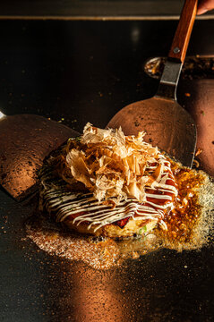 Cooking okonomiyaki on a teppan grill with metal spatulas