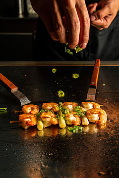 Chef garnishing grilled prawn skewers on a teppanyaki plate