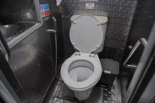 A compact restroom with steel walls and floors inside a train.