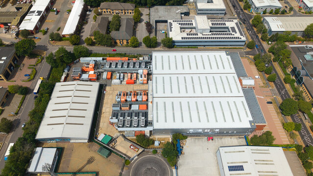 Aerial view of a data center facility with external cooling units for AI technology, surrounded by industrial buildings and green trees in Hemel Hempstead, England, United Kingdom.