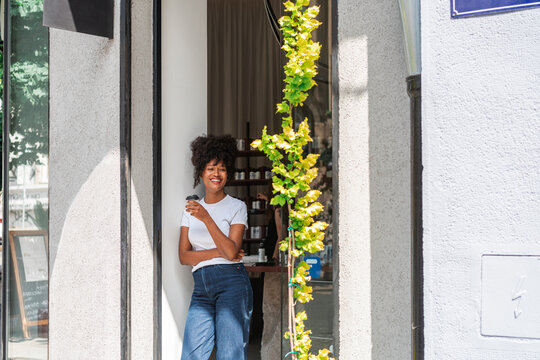 Smiling Young Woman Enjoying Coffee Outside a Cozy Urban Shop