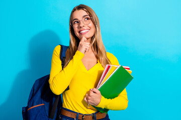 Naklejka premium Young student with backpack holding colorful notebooks and smiling thoughtfully against a bright blue background — education, study and back-to-school concept