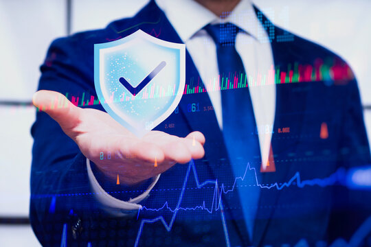 Businessman holding shield checkmark icon with stock market trading graph and chart overlay. Cyber security, financial risk management or investment protection concept.