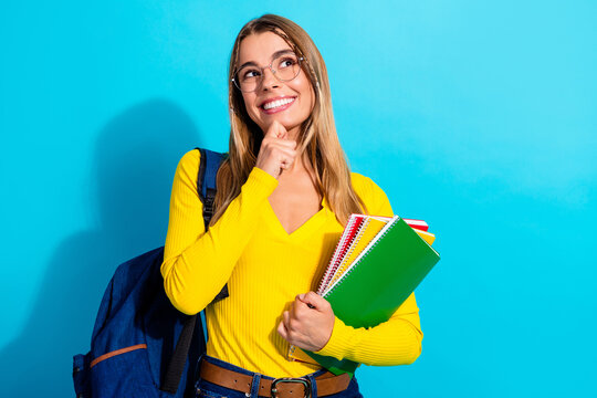 Young student with backpack holding colorful notebooks and smiling thoughtfully against a bright blue background &mdash; education, study and back-to-school concept