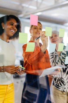 Women's group collaborating on ideas sticky notes glass board