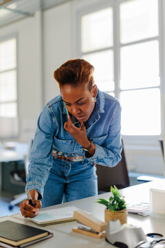 Woman with short hair communicating on phone while writing notes