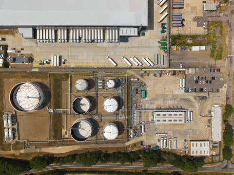 Aerial view of Buncefield Oil Depot and distribution centre featuring industrial storage tanks, a warehouse with parked HGVs, and a paved yard in Hemel Hempstead, England, United Kingdom.