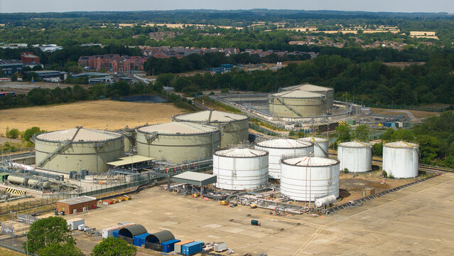 Aerial view of oil storage terminal and depot with large cylindrical storage tanks, industrial infrastructure, and surrounding green landscape in Hemel Hempstead, England, United Kingdom.