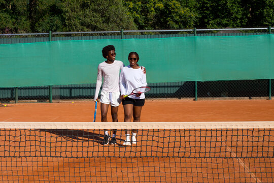 Black man and woman tennis players with rackets on court.