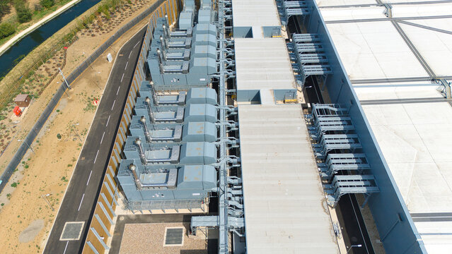 Aerial view of a hyperscale data center featuring rows of industrial air handling units and chillers on the roof, adjacent to a paved road and a canal in Hereford, England, United Kingdom.