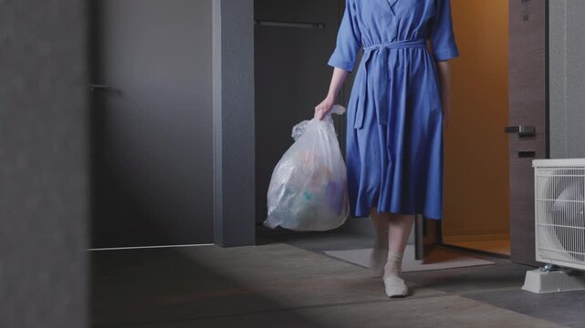 家庭ゴミを持って廊下を歩く女性