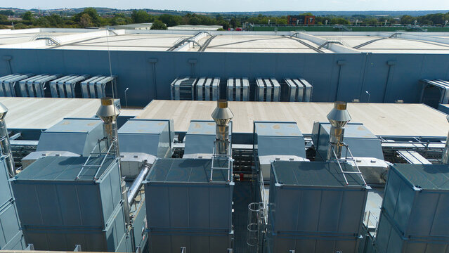Aerial view of a hyperscale data center rooftop with large industrial air handling units and chillers under a clear sky in Hereford, England, United Kingdom.