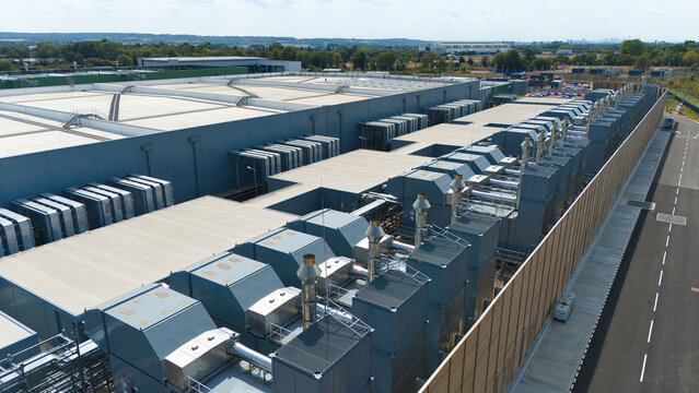 Aerial view of a hyperscale data center featuring rows of industrial air handling units and chillers on the roof, set within a large facility in Hereford, England, United Kingdom.