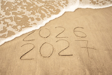 Fototapeta premium Inscription 2026 and 2027 numbers written on sand. New Year 2026 replace 2027. Concept on the sea beach
