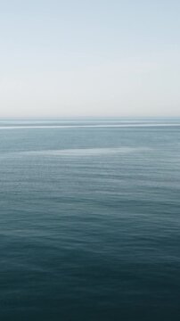Vertical aerial view over calm sea water surface. Sun glare. Abstract nautical summer ocean nature. Holiday, vacation and travel concept. Nobody. Weather and climate change