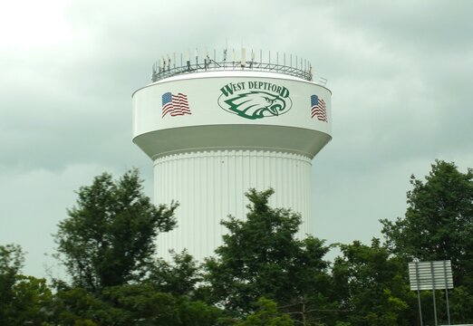 Gloucester County, New Jersey, U.S.A - Aug 17, 2026 - West Deptford water tower with eagle emblem and American flags rising above surrounding trees under a cloudy sky.