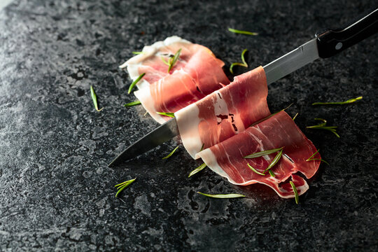 Sliced prosciutto and knife on a stone table.