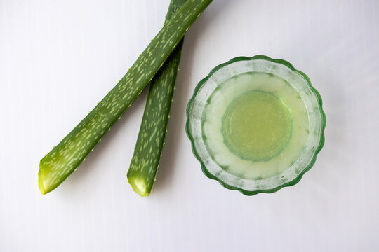 Fresh aloe vera gel juice extract in glass bowl with whole green leaves on clean white background. Homemade organic medicine used for skincare treatment. Top view.