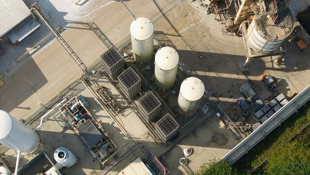 Aerial view of cryogenic storage tanks and gas vaporization systems at a glass manufacturing facility with industrial piping and concrete grounds in Harlow, England, United Kingdom.