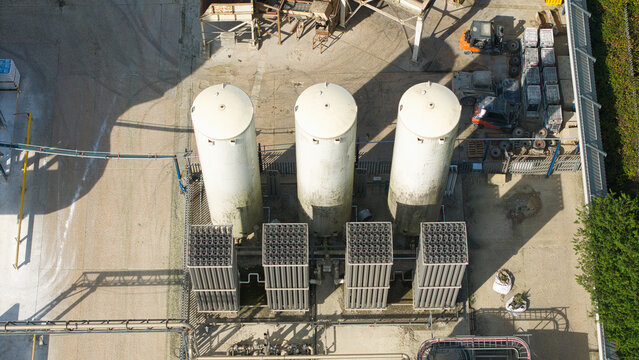 Aerial view of cryogenic storage tanks and gas vaporization systems at a glass manufacturing facility with industrial equipment and paved grounds in Harlow, England, United Kingdom.