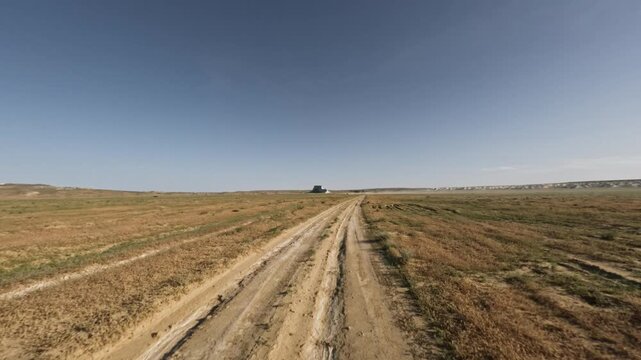 SUV driving on dirt road through open fields under clear blue sky
