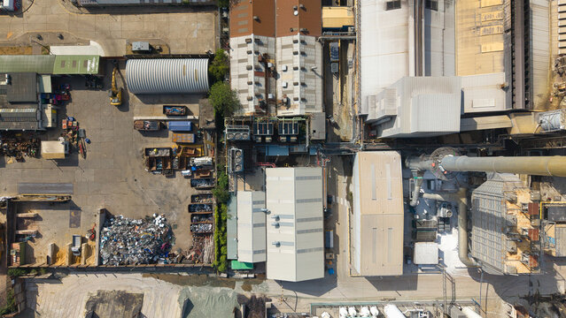 Aerial view of the O-I Glass Limited manufacturing facility featuring industrial buildings, metal rooftops, storage yards, and a tall chimney in Harlow, England, United Kingdom.