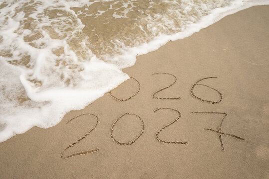 Inscription 2026 and 2027 numbers written on sand.  New Year 2026 replace 2027. Concept on the sea beach